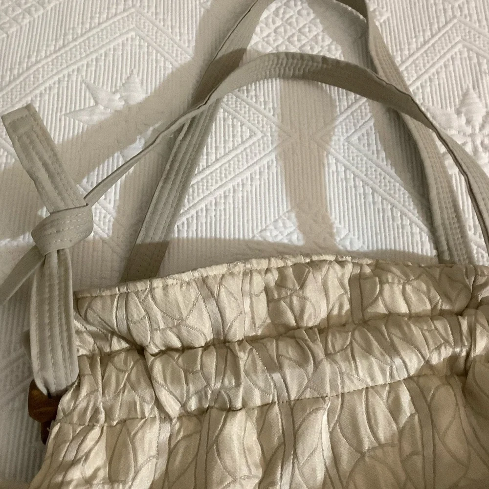 FABRIC SHOULDER BAG WITH OUTSIDE SURROUNDING POCKETS IN A CREAM AND TAUPE COLOR.